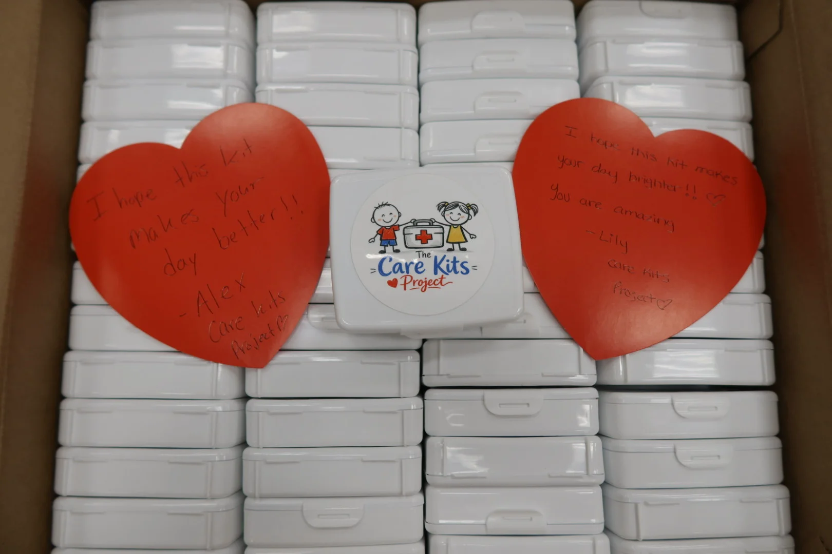 Finished care kit cases packed in a box with two handwritten heart notes on top